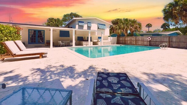 A backyard with a swimming pool, lounge chairs, and a wooden fence. - Mermaids' BeachHouse: Walk2Beach • Pool • KingBed (Cocoa Beach)