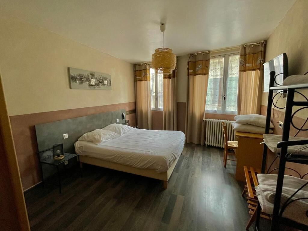 Ett hotellrum med en säng, ett skrivbord, en stol, ett element och ett fönster med gardiner.