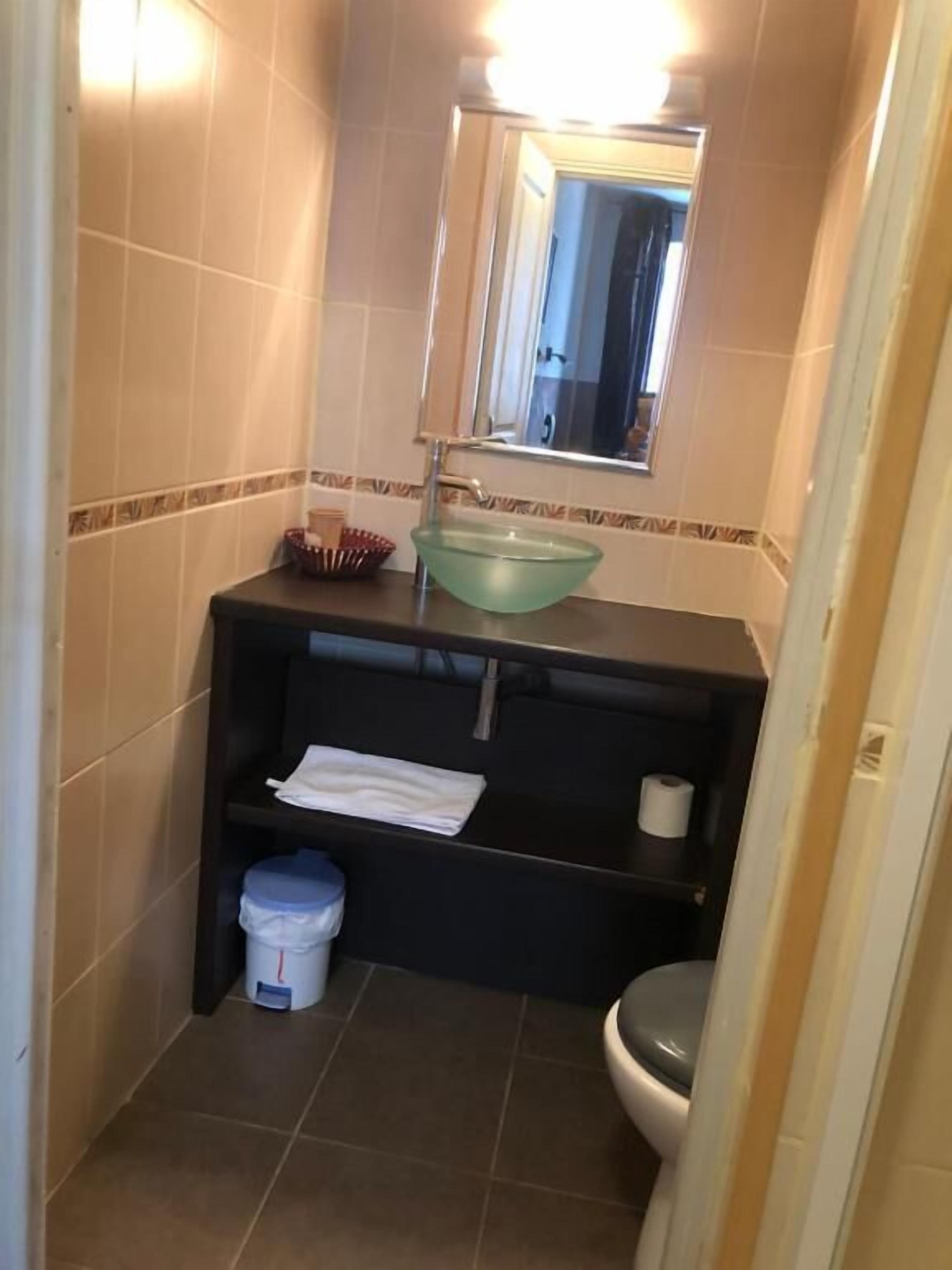 Un baño pequeño con lavamanos, espejo, inodoro y un cubo de basura.