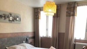 A hotel room with a large bed, a wooden floor, a window with curtains, and a hanging light fixture.