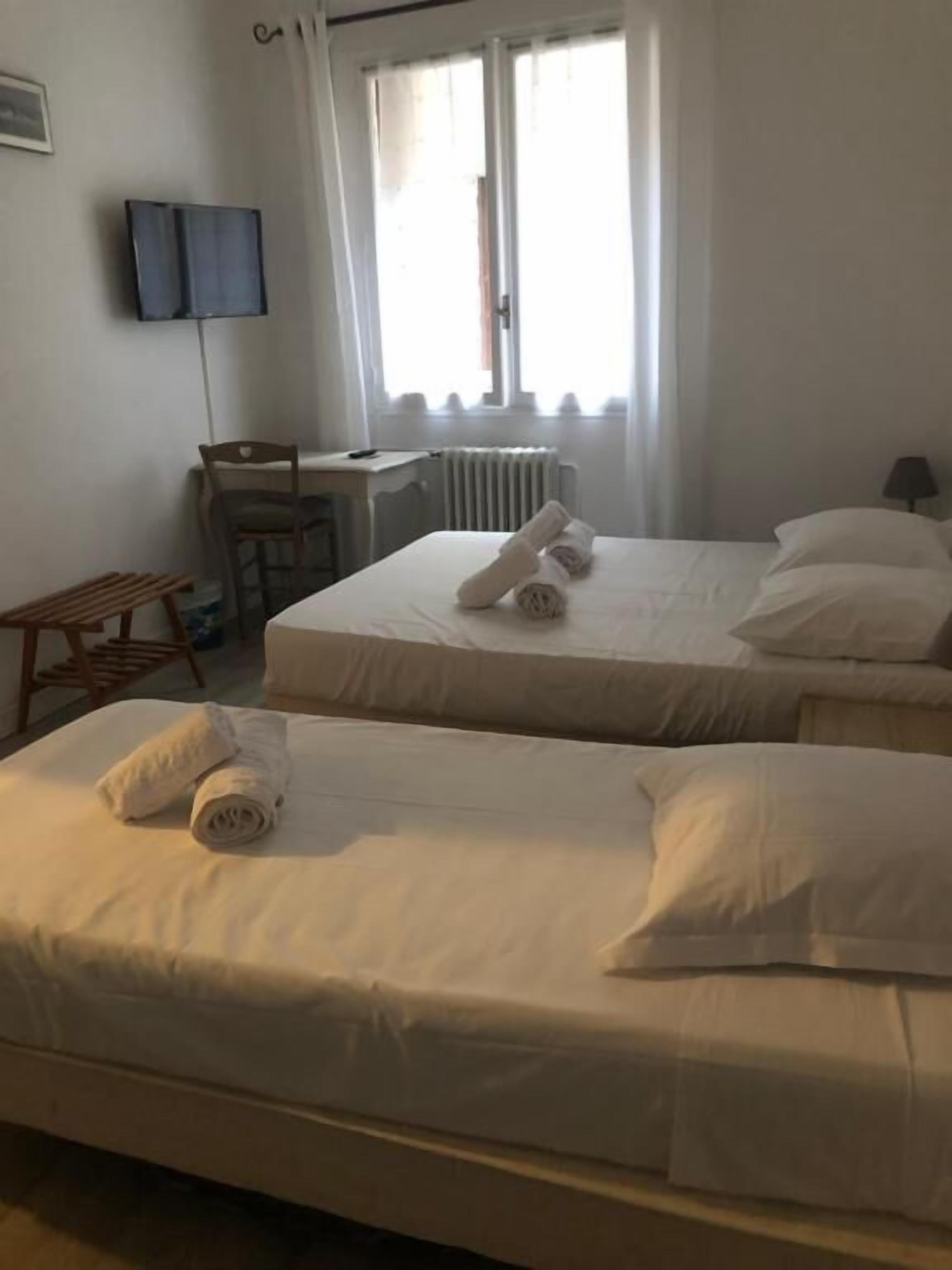 Une chambre d’hôtel avec deux lits, un bureau, une chaise et un téléviseur fixé au mur.