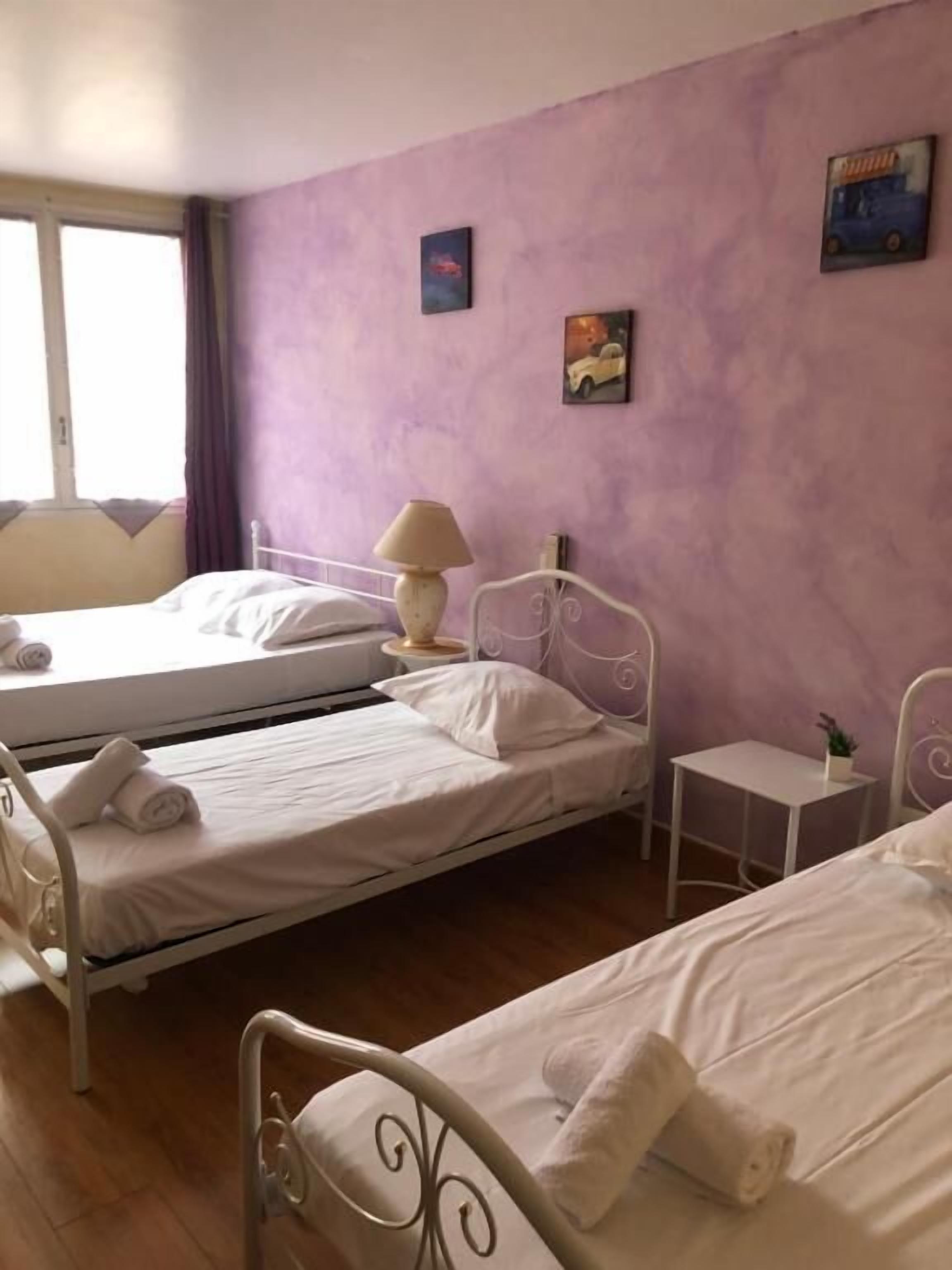 Una habitación de hotel con dos camas, una mesita, una lámpara y una ventana con cortinas.