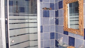 A bathroom with a shower, a glass door, a mirror, and a shelf with toiletries.