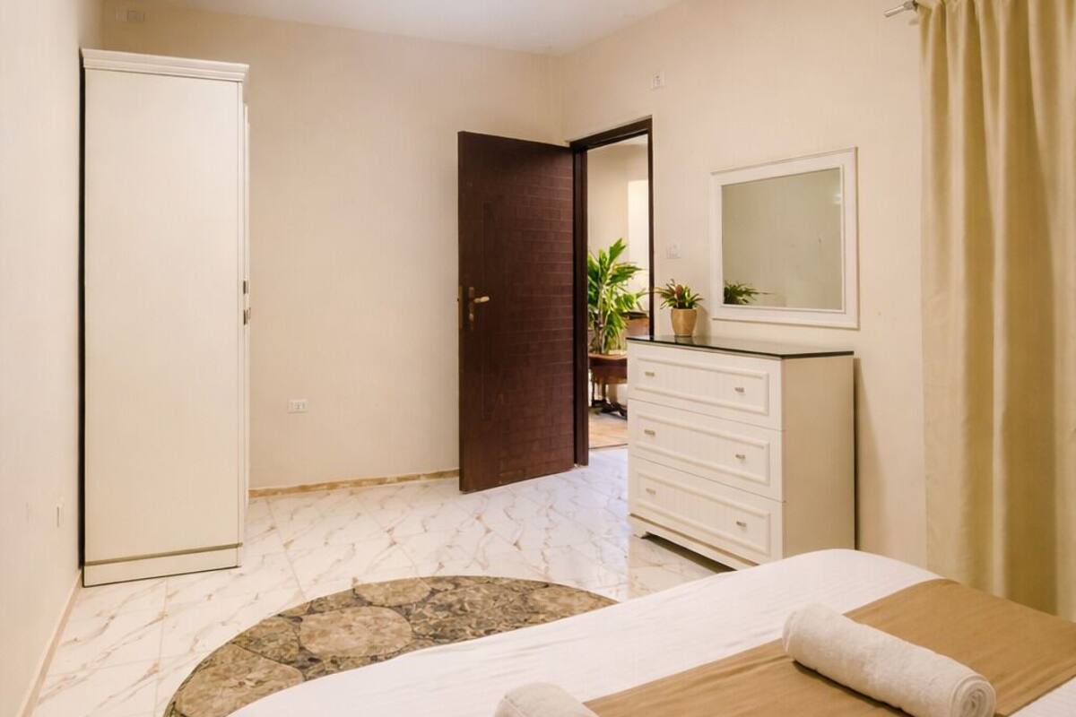 A hotel room with a bed, a dresser, a mirror, and a door leading to another room.