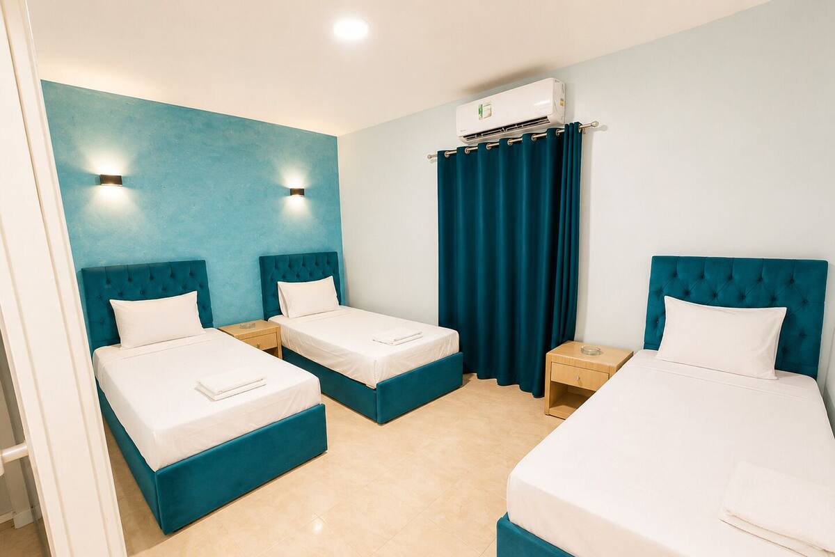 A hotel room with two single beds, a double bed, a bathroom with a shower, and an air conditioning unit.