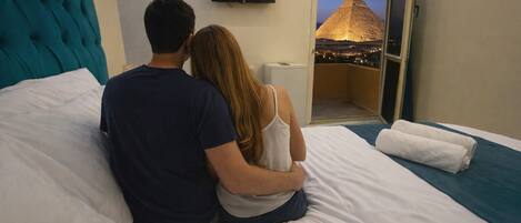 Una coppia seduta su un letto con vista su una piramide attraverso una porta aperta.