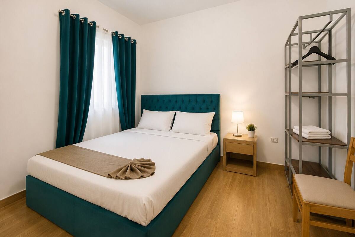 A hotel room with a bed, a nightstand, a chair, a wardrobe, and a window with curtains.