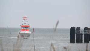A boat with a red and white cabin moving through a body of water near a pier with multiple pillars. - Heckenrose 5 EG Rechts (Norddorf auf Amrum)