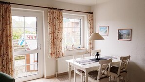 A dining area with a table and chairs, a radiator, and a window with curtains. - Heckenrose 5 EG Rechts (Norddorf auf Amrum)