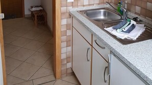 A kitchen with a sink, cabinets, and a tiled backsplash. - Heckenrose 5 EG Rechts (Norddorf auf Amrum)