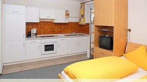 Une petite chambre comprenant un lit, une kitchenette et un téléviseur.