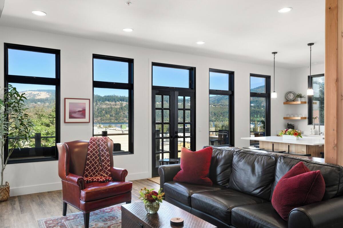 A living room with a leather sofa, a red armchair, and a large window overlooking a scenic landscape.
