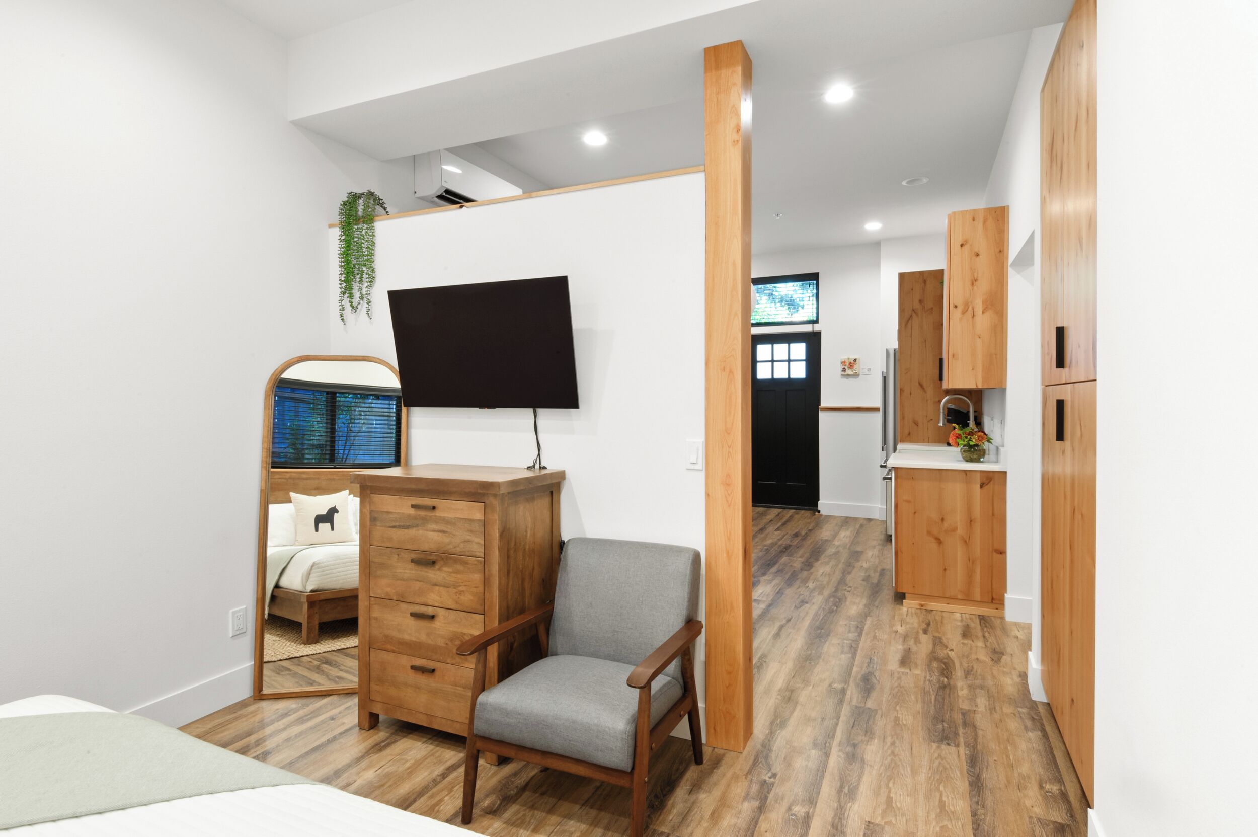 Una habitación moderna con un armario de madera, una silla gris, una cama con cabecera blanca y un televisor de pantalla plana montado en la pared.