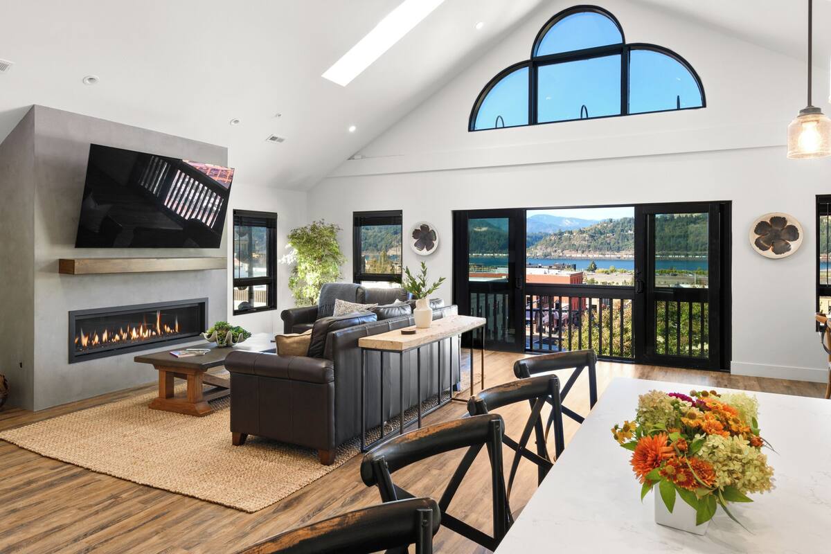 A spacious living room with a fireplace, a large flat-screen TV, comfortable seating, and a view of the outdoors.