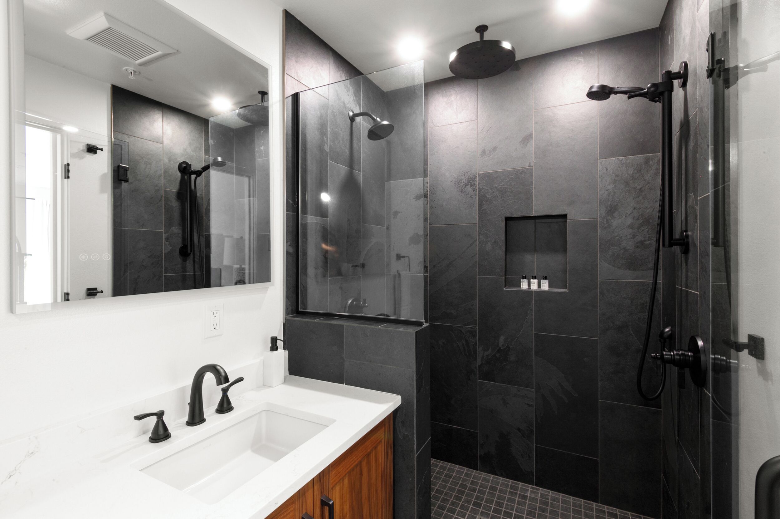 Une salle de bain moderne avec un lavabo blanc, des accessoires noirs et des murs recouverts de carreaux foncés.