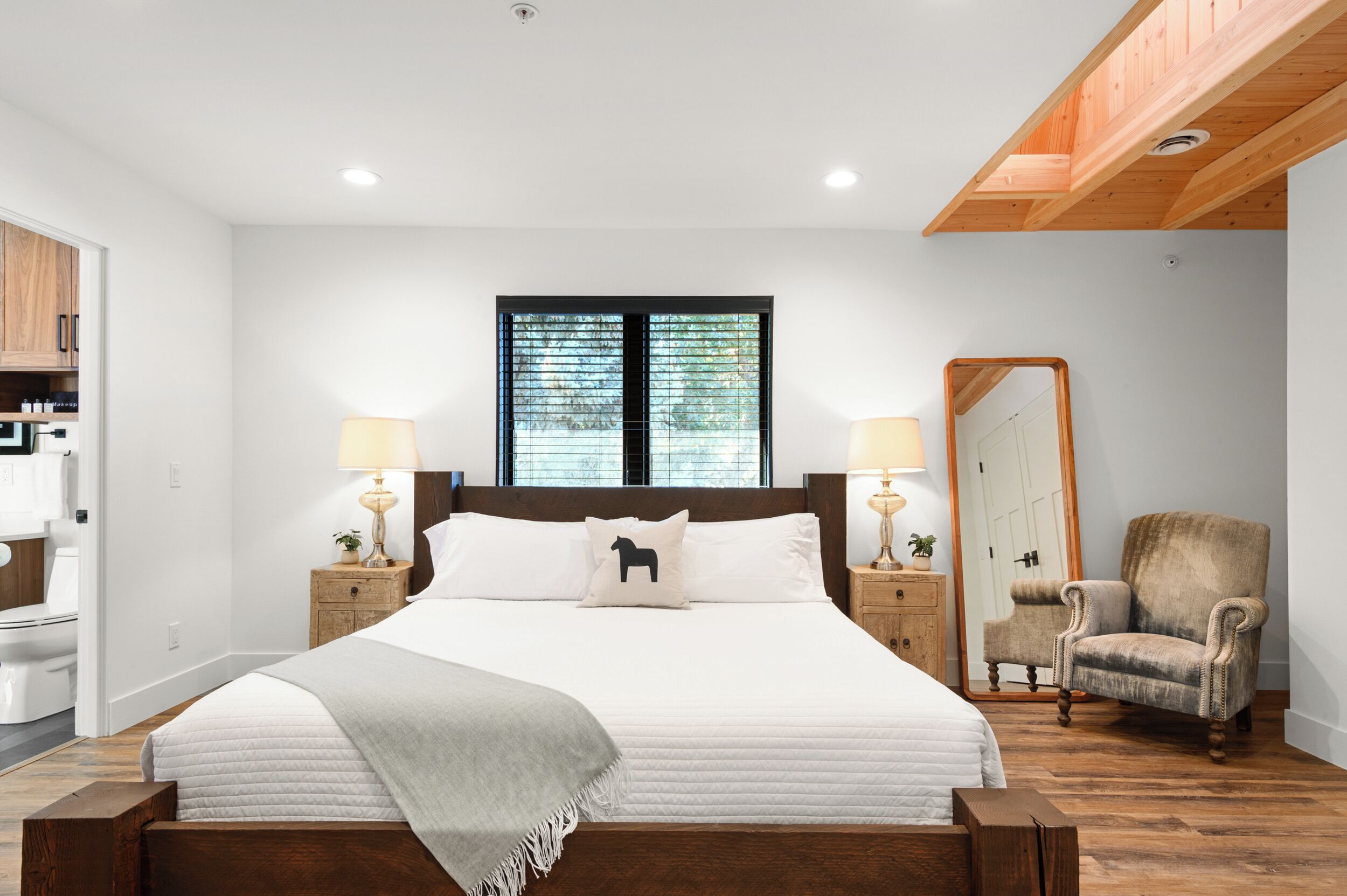 A bedroom with a large bed, wooden headboard, two bedside lamps, a mirror, and a chair.