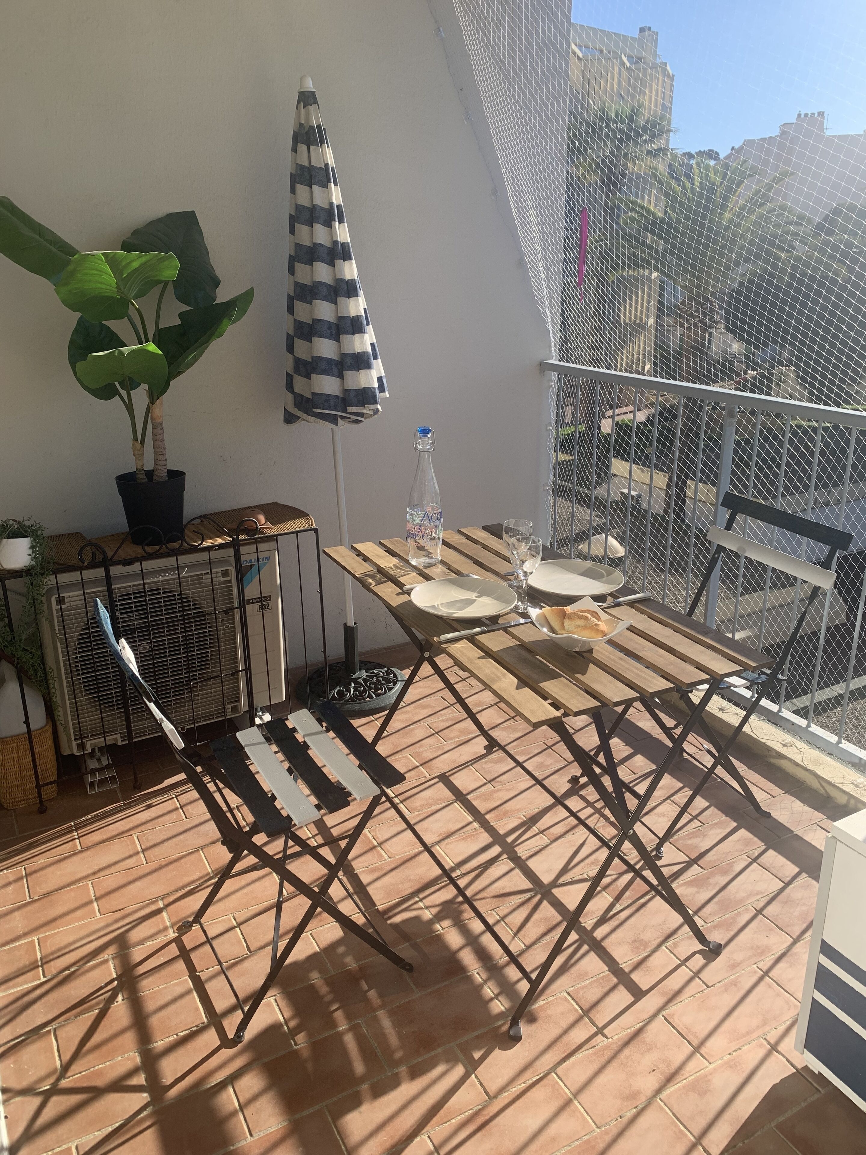 Ein kleiner Balkon mit Tisch, Stühlen, einem Blumentopf, einer Flasche und einem Sessel.