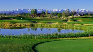 Un parcours de golf avec un étang, des maisons et, au loin, des montagnes aux sommets enneigés.