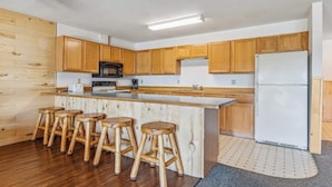 A kitchen with wooden cabinets, a central island with stools, a refrigerator, and a microwave. - Lakeside Condo #19 4BR 4BA Timberlane Resort (Park Rapids)