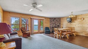 A cabin interior with a sofa, chairs, a table, a ceiling fan, and a stone wall. - Lakeside Condo #19 4BR 4BA Timberlane Resort (Park Rapids)