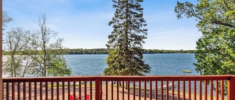 Une terrasse en bois avec une balustrade donnant sur un lac, entourée d’arbres.