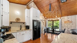 Une cuisine moderne avec des meubles blancs, un réfrigérateur noir et un coin repas comprenant une table et des chaises.