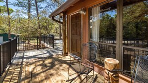 Une terrasse en bois avec une porte vitrée donnant sur un espace abrité, le tout entouré d’arbres.