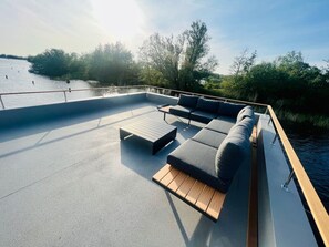 Terraza exterior con sofá y mesa, con vista a un cuerpo de agua y rodeada de vegetación.