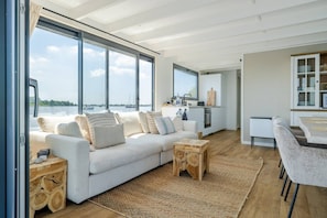 Ett modernt vardagsrum med ett stort fönster, en soffa, ett soffbord och en köksdel.