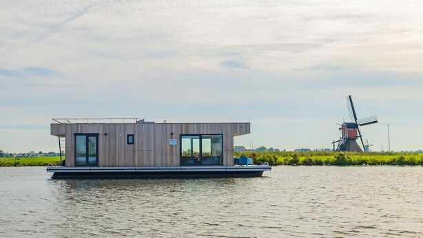 Uma casa flutuante moderna com telhado plano, grandes janelas e uma pequena área de deck.