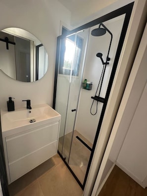 Ett badrum med en dusch som är avskärmad med glasväggar, ett vitt handfat med en svart kran och en spegel ovanför handfatet.