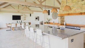 Una cocina amplia con una isla grande, taburetes blancos de bar y un salpicadero de piedra.