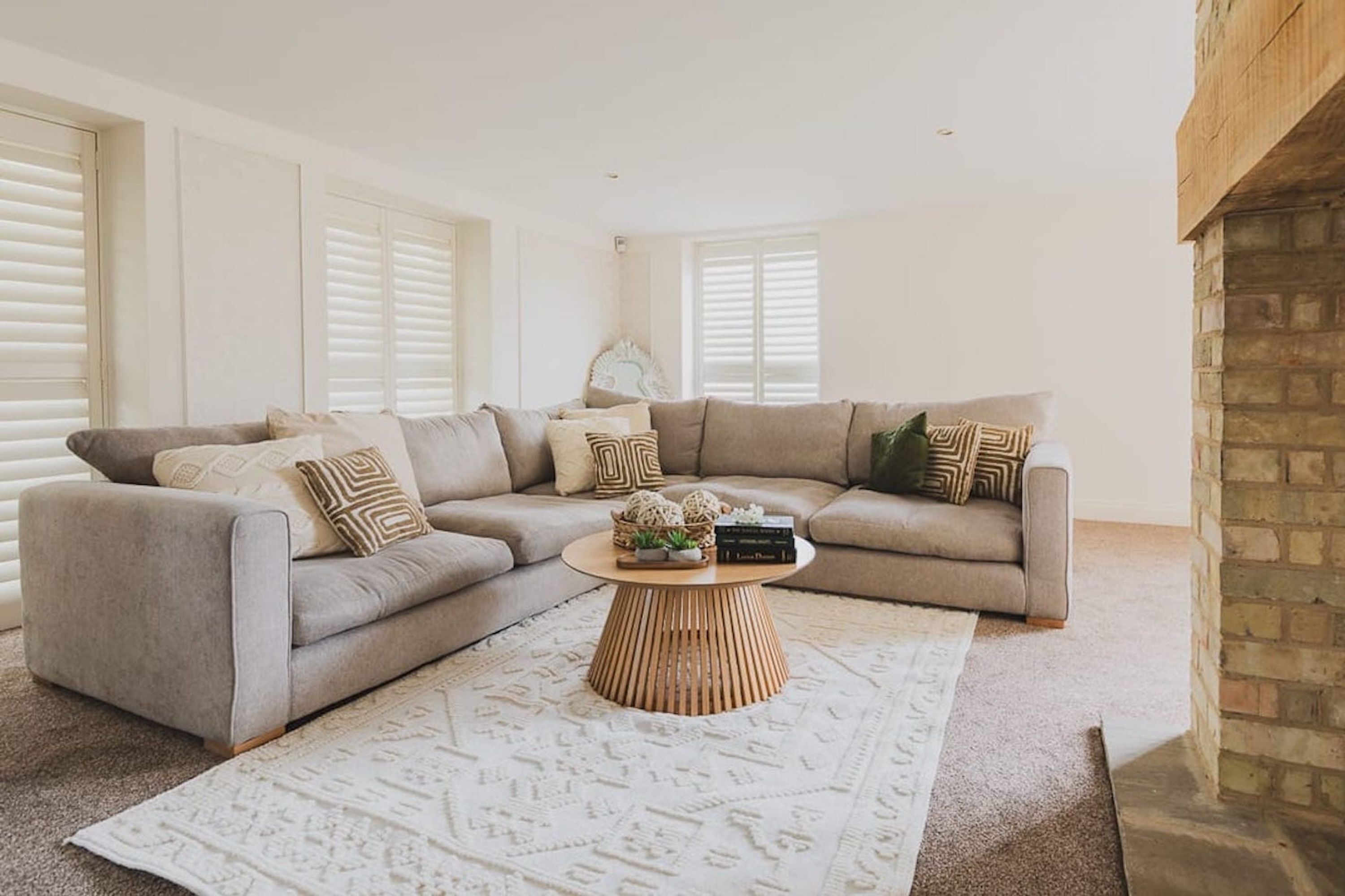 Ein Wohnzimmer mit einem grauen Ecksofa, einem runden Couchtisch aus Holz und gemusterten Teppichen.