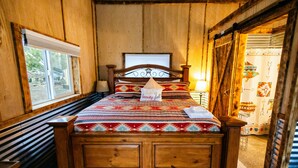 Een bed met houten frame, een beddengoed met patroon, een kussen met een motiverende quote, en een raam met jaloezieën.