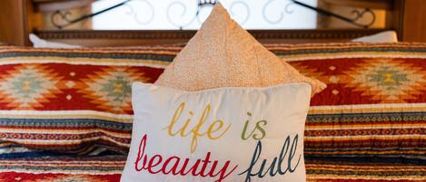A bed with a decorative pillow featuring the text 'life is beauty full' and a patterned bedspread.