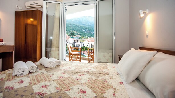 Un dormitorio con cama, armario de madera, balcón con sillas y vista a la montaña.