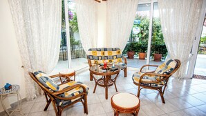 Una habitación soleada con muebles de mimbre, una mesa de vidrio y vistas a la vegetación exterior.
