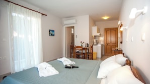 Una habitación de hotel con una cama, una silla, una mesita y una kitchenette al fondo.