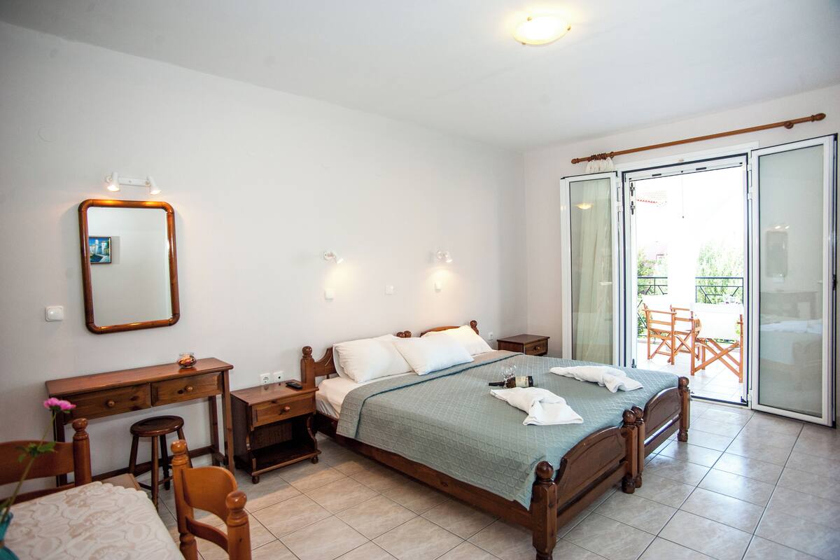 A bedroom with a bed, bedside tables, a desk, a chair, a mirror, and a sliding glass door to an outdoor area.