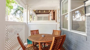 Une terrasse couverte avec une table et des chaises en bois, une clôture en treillis blanche et une vue sur le quartier.