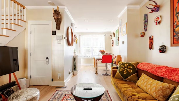 Un salon moderne avec un canapé, une table basse et un téléviseur. Un escalier se trouve à gauche, et un coin repas avec une table et des chaises est aménagé.