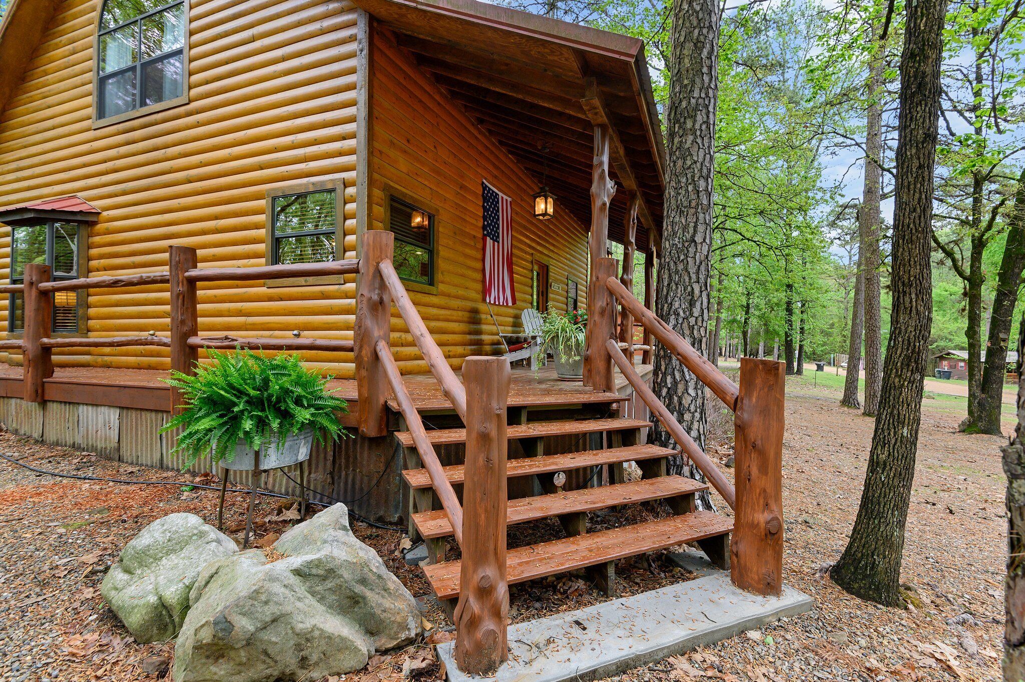A log cabin with a wooden staircase leading to a porch, surrounded by trees.