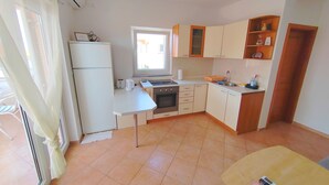A compact kitchen with a refrigerator, oven, and sink. There is a window providing natural light and a view of the outside. - Sea View Apartment Luka (Novalja)