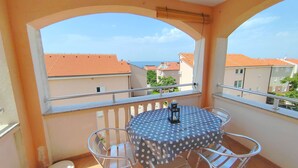 A balcony with a round table and chairs, a view of buildings, and a railing. - Sea View Apartment Luka (Novalja)