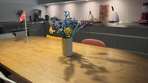 Eine moderne Küche mit einem Holztisch, einer Vase mit bunten Blumen und einer großen Pendelleuchte.