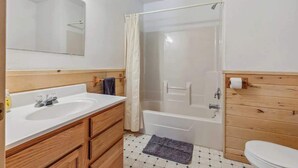 Une salle de bain avec un meuble-lavabo en bois, un grand miroir, une baignoire et des toilettes.