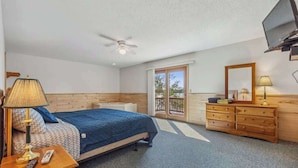 Une chambre à coucher avec un lit, un ventilateur de plafond, une télévision, une commode et une porte-fenêtre donnant sur un balcon.