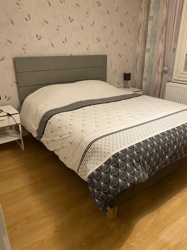Un dormitorio con cama, suelo de madera y mesita de noche.