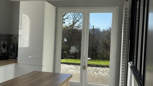 Una cocina moderna con encimera de madera, armarios blancos y vistas a un patio exterior a través de puertas de vidrio.