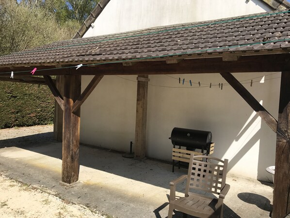 A covered outdoor seating area with a wooden bench and a grill.